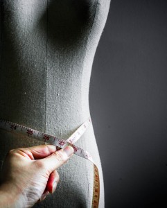 A tailor uses a tape measure to measure the waste of a dress form