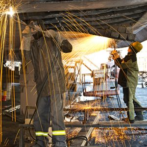 A maritime worker grinds the hull of a ship in drydock