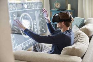A man on a sofa interacts with a virtual screen using virtual reality goggles.