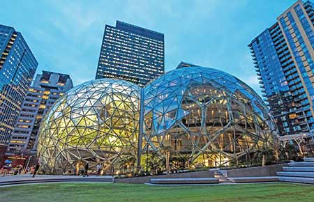 Amazon's Spheres gevuld met gebladerte op de voorgrond met daarachter het Doppler-gebouw van het bedrijf.