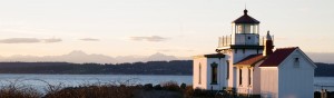 A Washington State lighthouse along the Puget Sound as the sun sets over the Olympic Mountains
