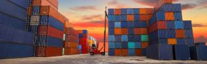 A forklift stacks containers on a dock as the sun rises