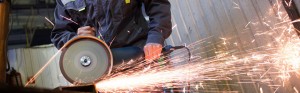 An operator works a hand grinder on a piece of metal, sending off a shower of sparks