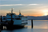 A Washington State ferry departs a dock as the sun sets over Puget Sound