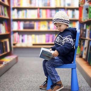 A small child reads a book, seated in a bookstore aisle
