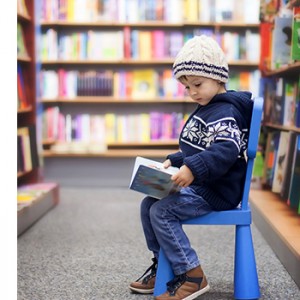 A child sits in a bookstore aisle reading a book